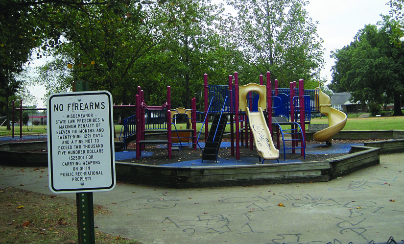 Uma foto de uma placa que diz “Sem armas de fogo”. Um playground pode ser visto ao fundo.