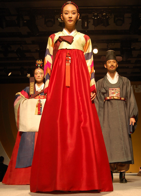 A korean woman in a hanbok, a wrapped dress with an empire waist and a floor-length, red a-line underdress.