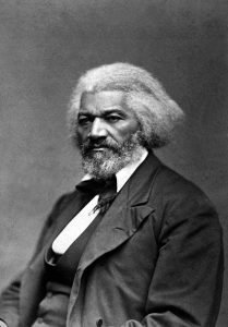 Black and white image of Frederick Douglass sitting wearing a black coat and tie.