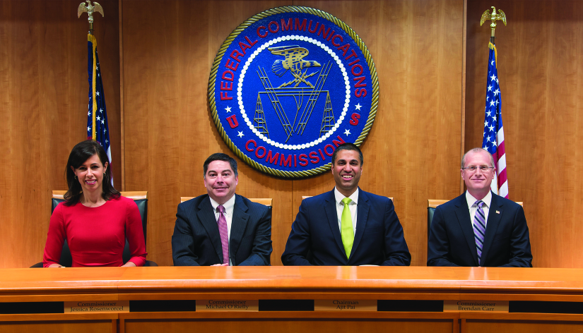 An image from left to right of Ajit Pai, Mignon Clyburn, Chairman Tom Wheeler, Jessica Rosenworcel and Michael O’Rielly seated in front of a large circular banner reading “Federal Communications Commission”.