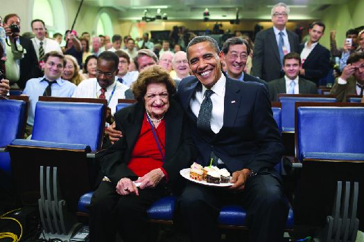 巴拉克·奥巴马和海伦·托马斯坐着的照片。 奥巴马拿着一盘蛋糕。