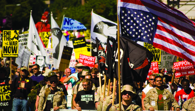 一群人的照片，其中一些人手持旗帜和标志。 其中一个标语写着 “立即结束战争”，另一个标语写着 “支持部队，结束战争”。