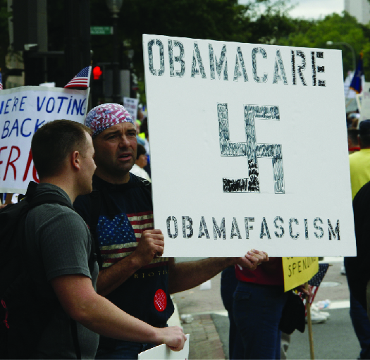 一张手持标语的人的图片，上面写着 “奥巴马医改奥巴马法西斯主义”，并带有十字记号的标语。
