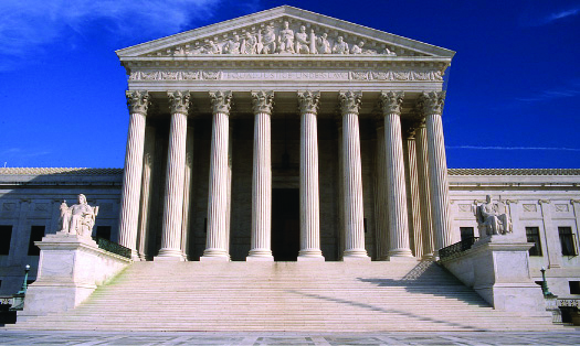 Une image du bâtiment de la Cour suprême. Au premier plan, un escalier est entouré de statues de chaque côté, menant à un portique. Le portique est coiffé d'un toit soutenu par plusieurs hautes colonnes.
