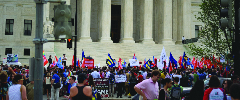 صورة لمجموعة من الأشخاص يقفون أمام مبنى. بعض الناس يحملون لافتات.