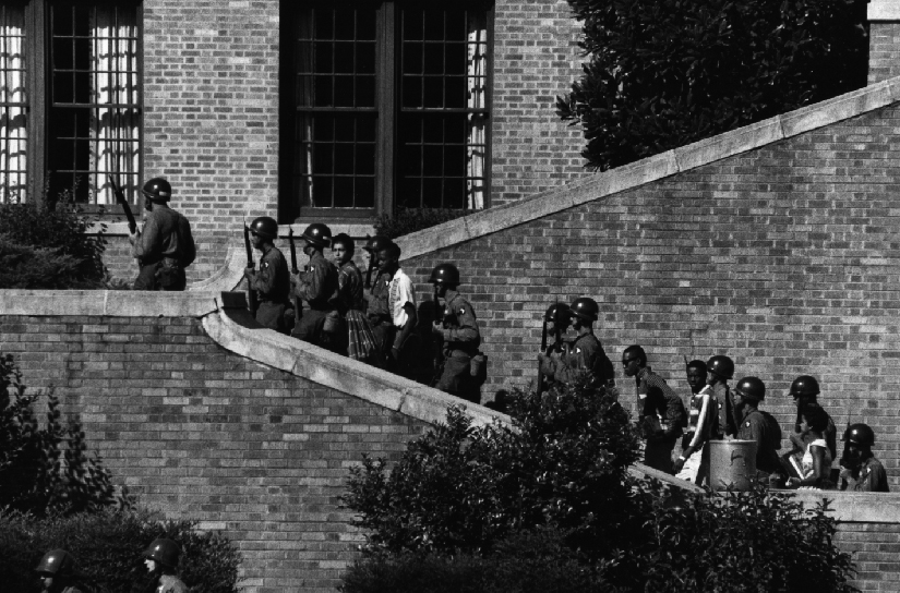 Image de personnes armées portant des casques, escortant plusieurs enfants dans un escalier en brique.