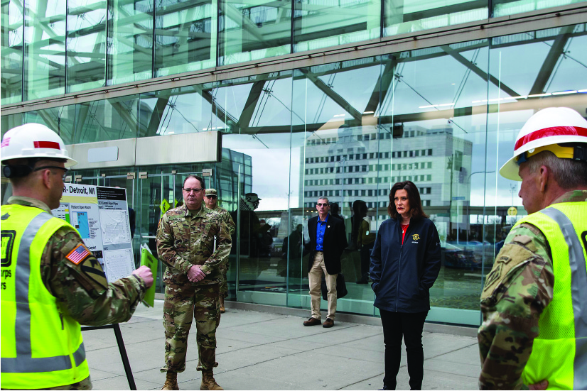 一张照片显示格蕾琴·惠特默站在城市建筑物外面，听取一个身穿军装的人的简报。 另外两名身穿军装的人和一名便衣人员出席了简报会。