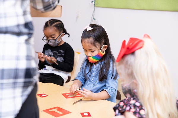 Los niños trabajan en una mesa usando plantillas y palos para explorar la formación de letras.