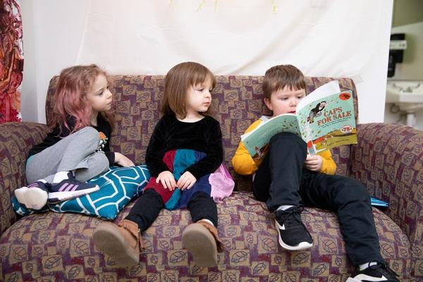 Tres niños leen juntos en un sofá.