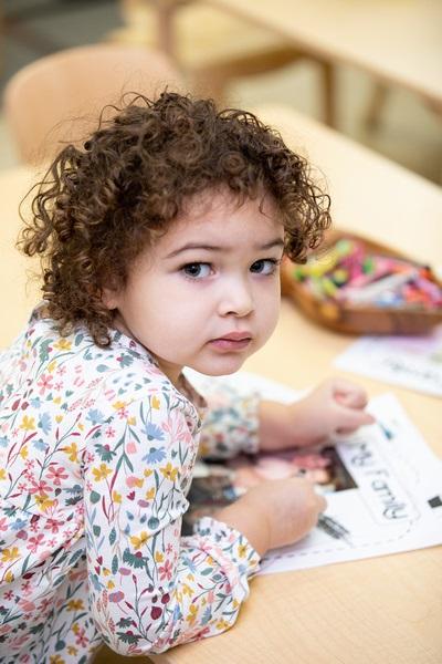 Una niña usa un crayón para dibujar un cuadro junto a una fotografía de su familia