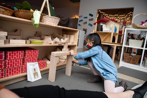 A child kneels on the carpet building a block structure in the block area.