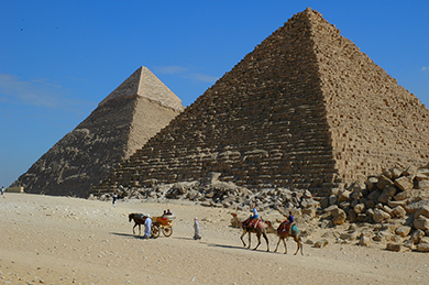 الصورة عبارة عن صورة لأشخاص يركبون الإبل أمام هرمين في مصر.
