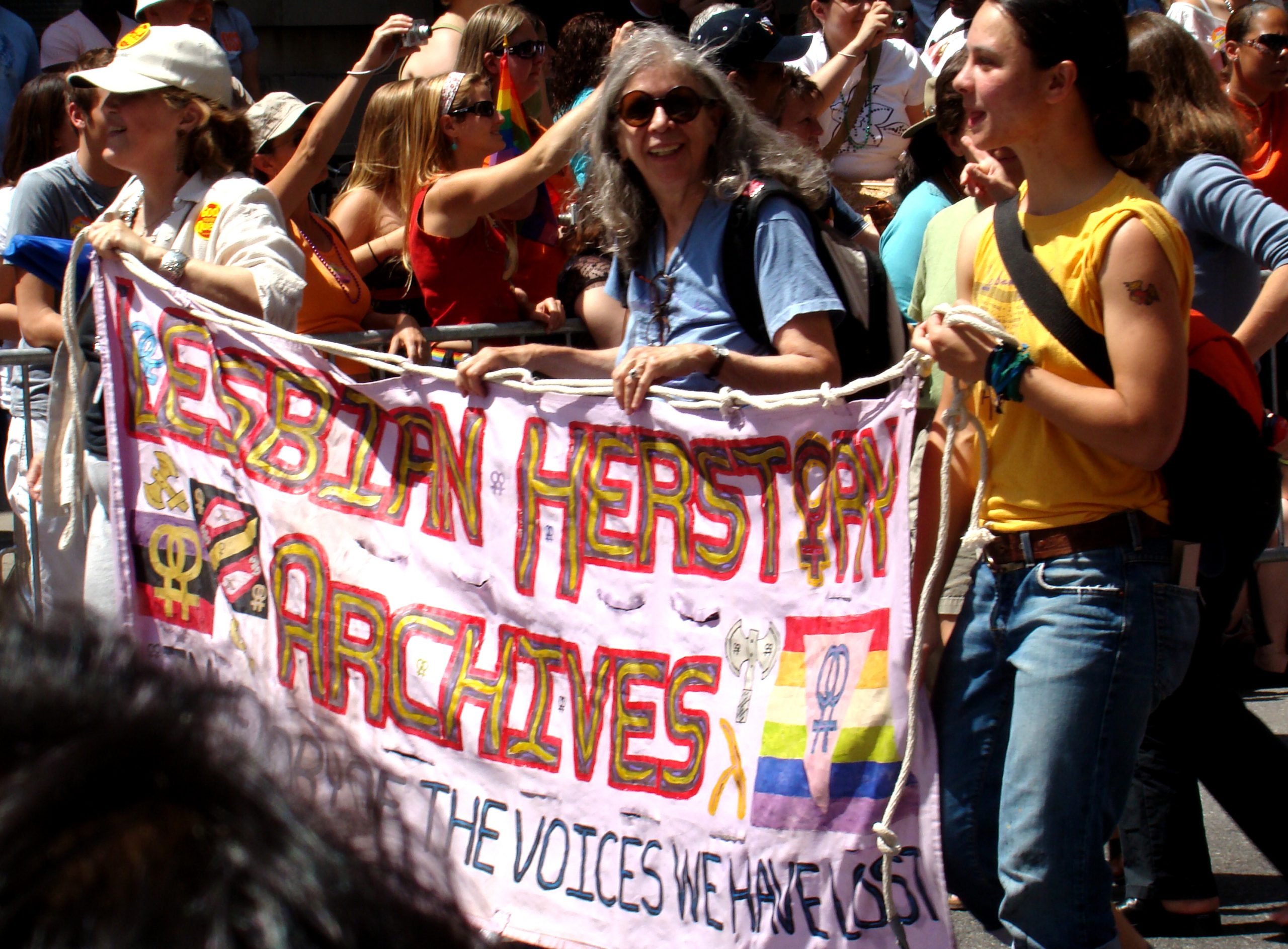 A crowd holds up a banner that says "Lesbian Herstory Archives."