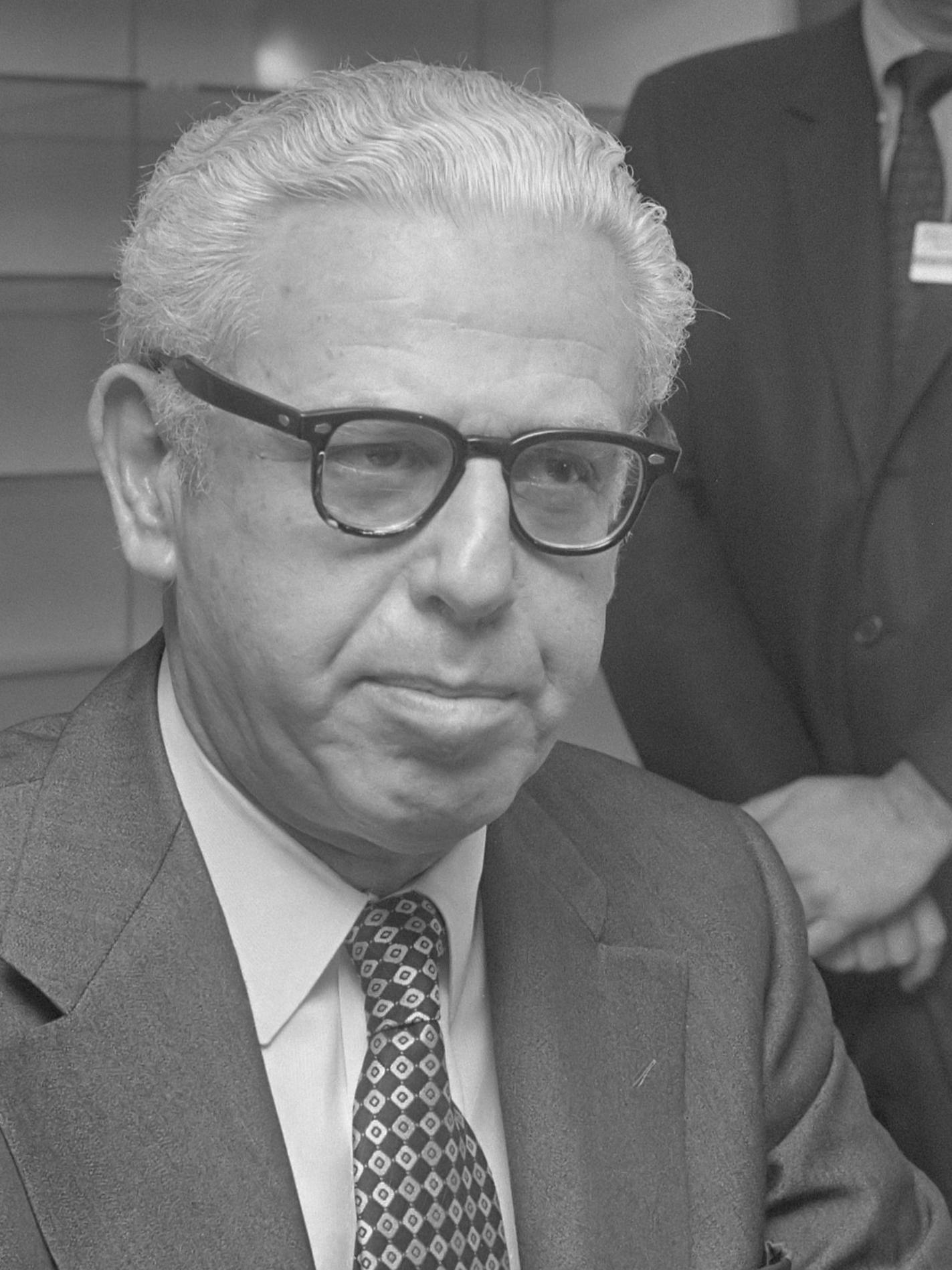 Black-and-white photograph of a man in a suit with glasses.