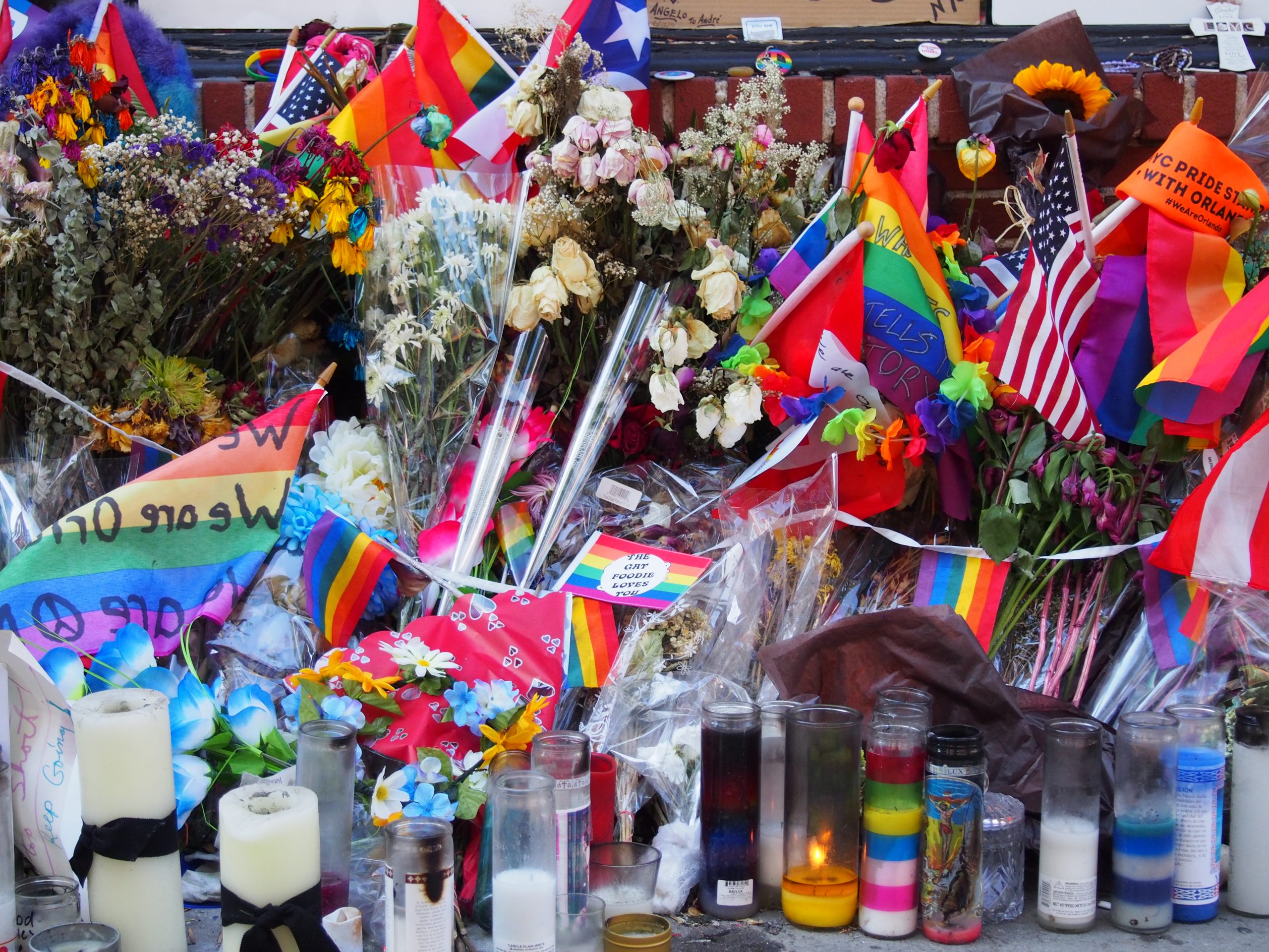 Rainbow flags surrounded by candles and flowers.