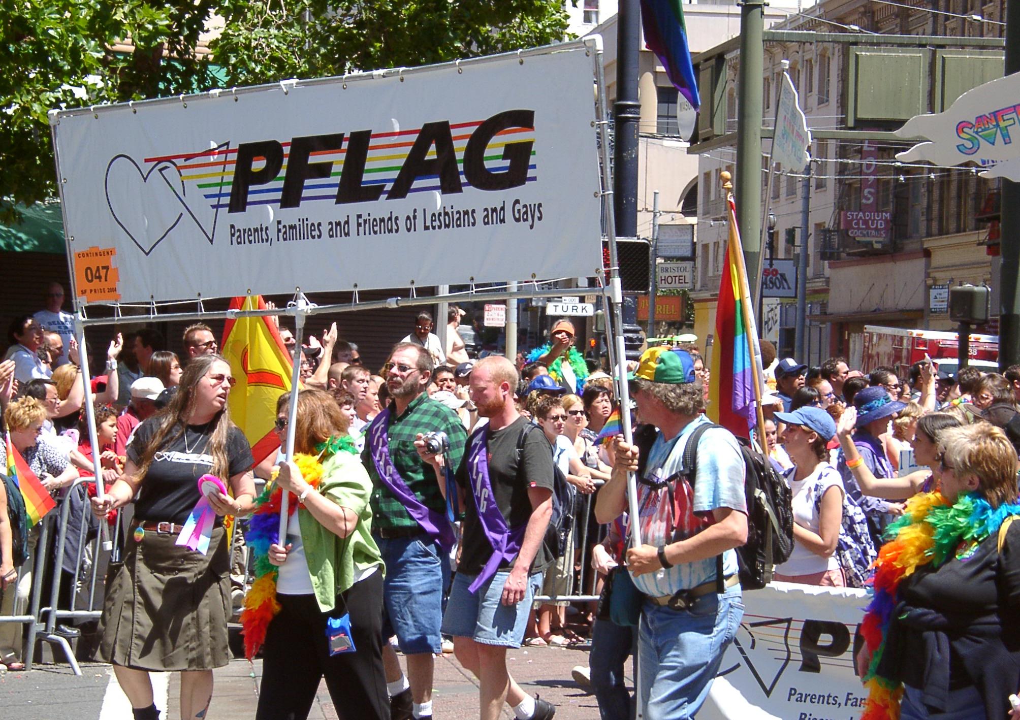 A crowd holds up a sign that says "PFLAG Parents, Families and Friends of Lesbians and Gays."