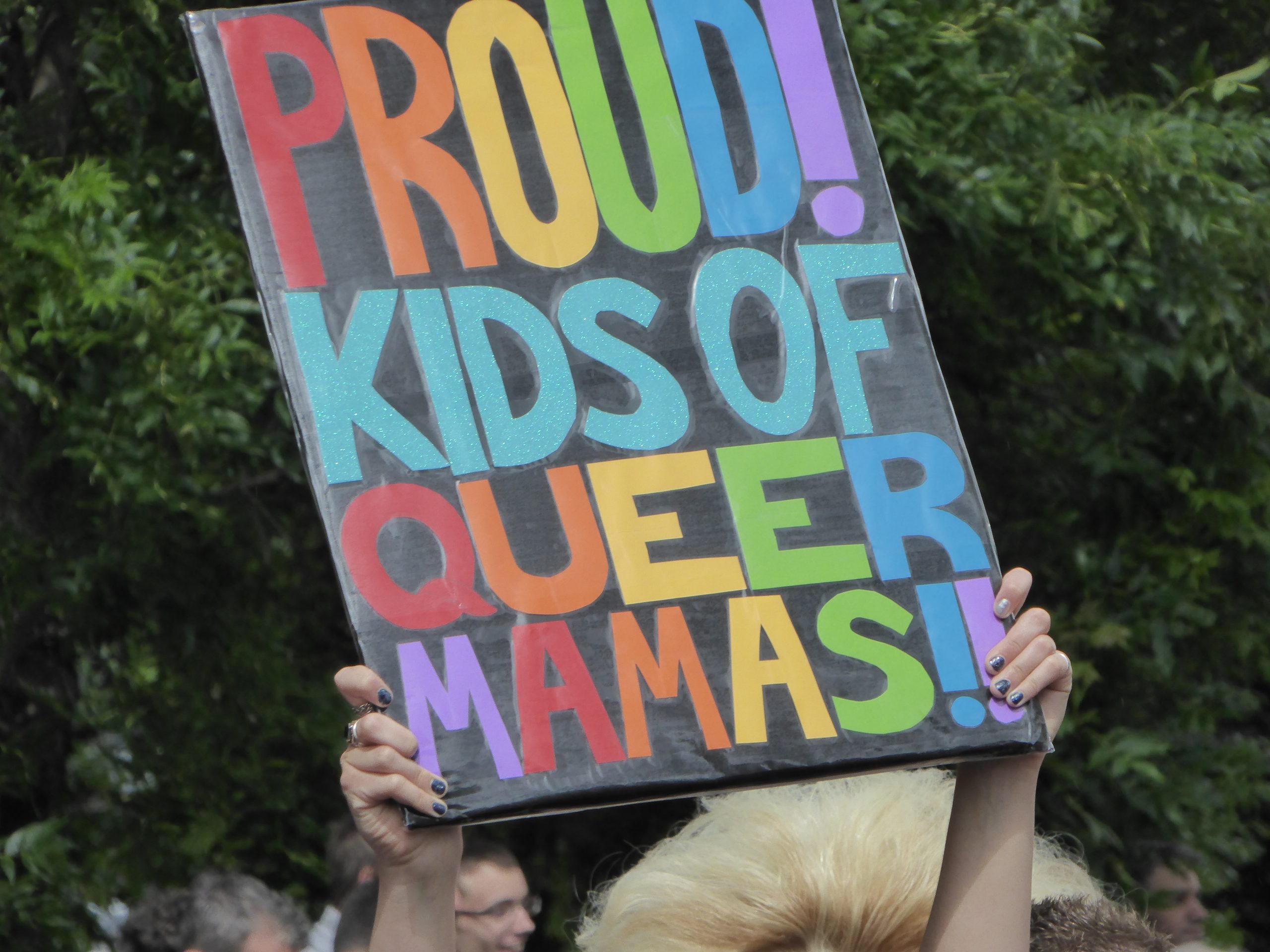 A sign is held up that says "PROUD! KIDS OF QUEER MAMAS!!"