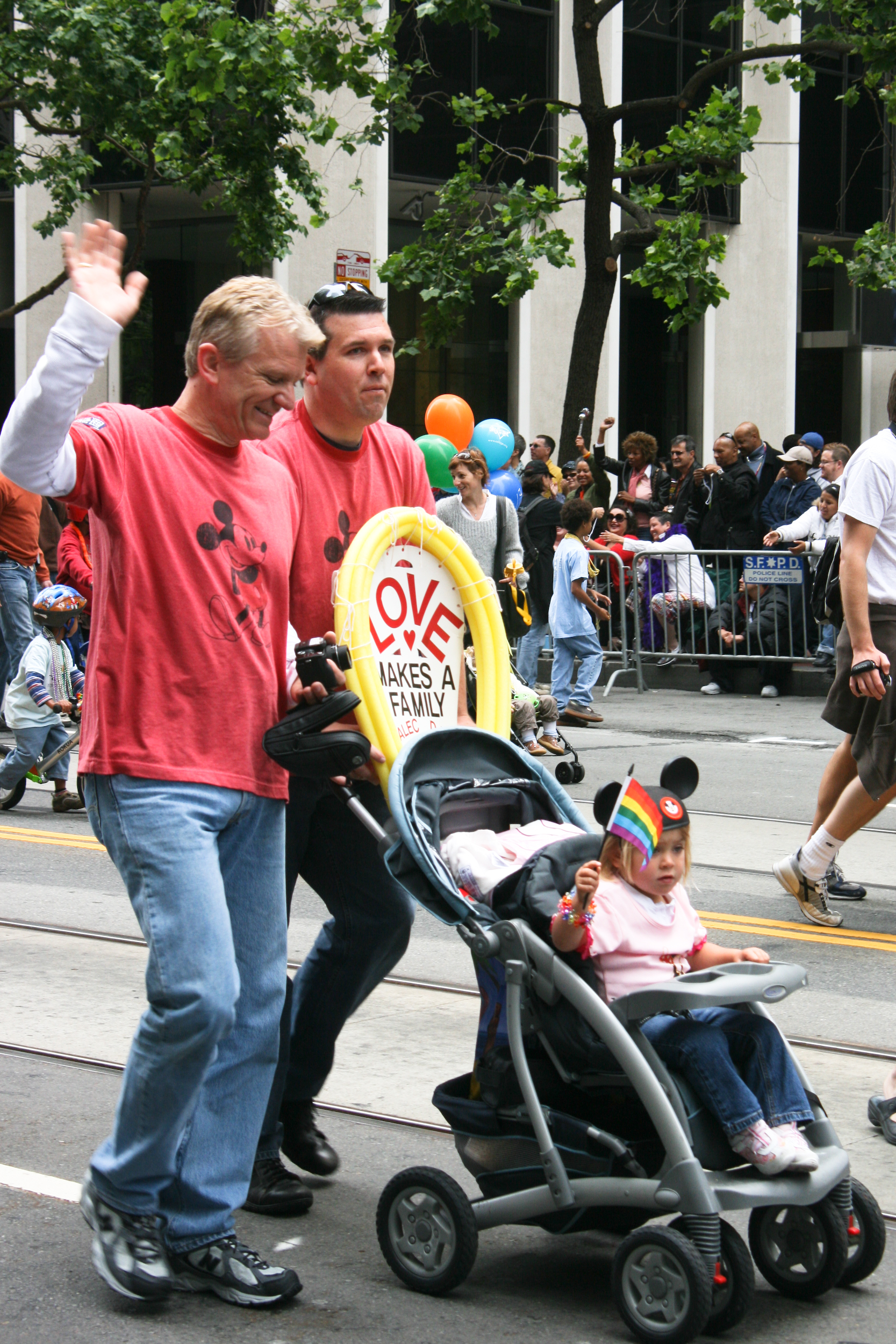 Two men push their child in a stroller at a parade.