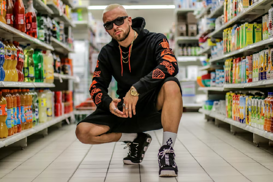 Person wearing a hoodie and dark glasses squatting down in the aisle of a store