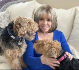Victoria has dark blonde hair and is wearing a blue top sitting with her Welsh Terriers on her lap. 