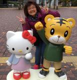 Kim with short black hair and glasses is standing next to Hello Kitty statues