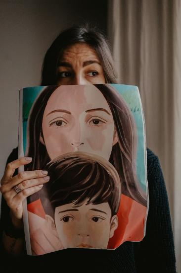 A person holding a painting of themselves as a teen and a child.