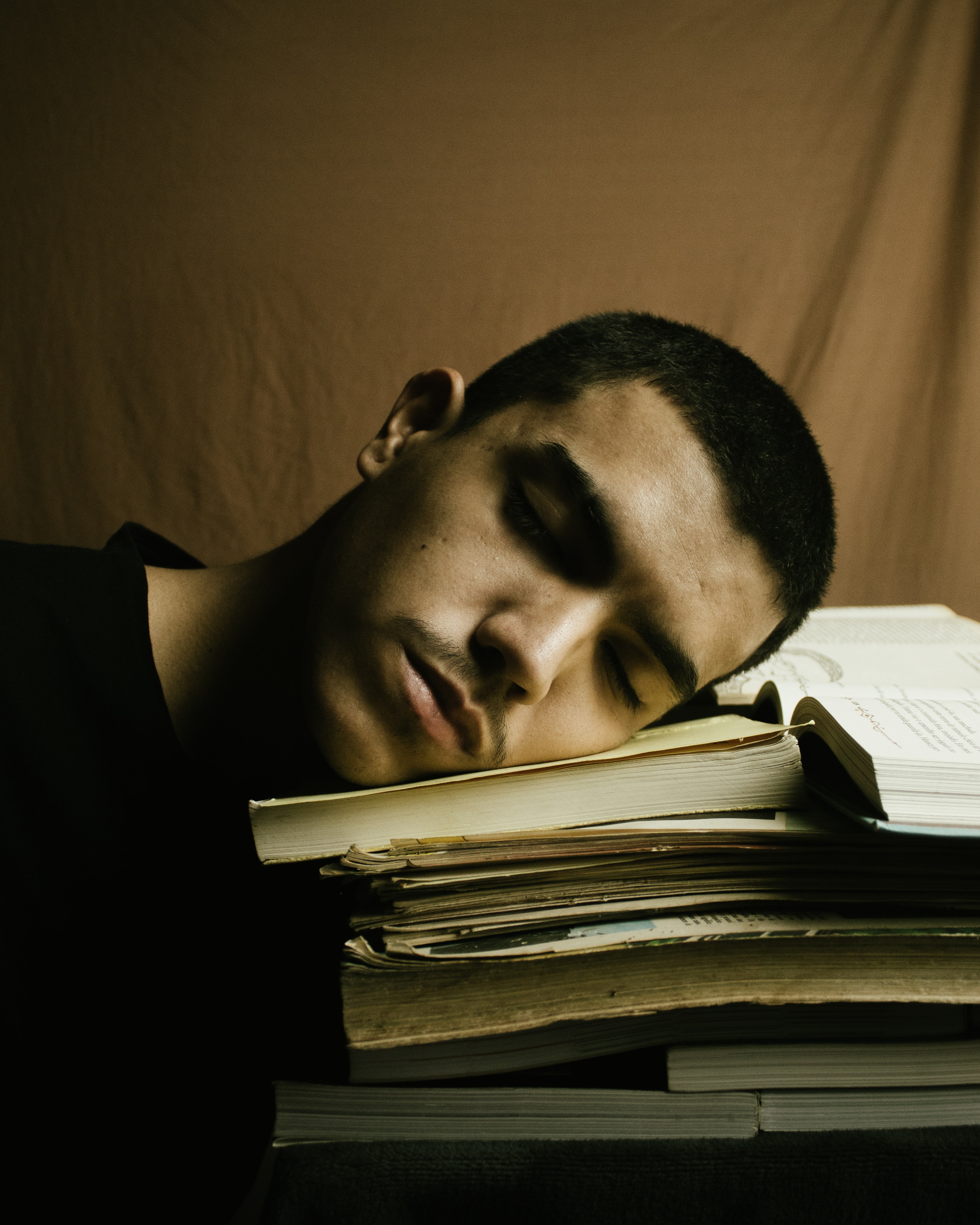 close up of a man in a black shirt, asleep on an open book