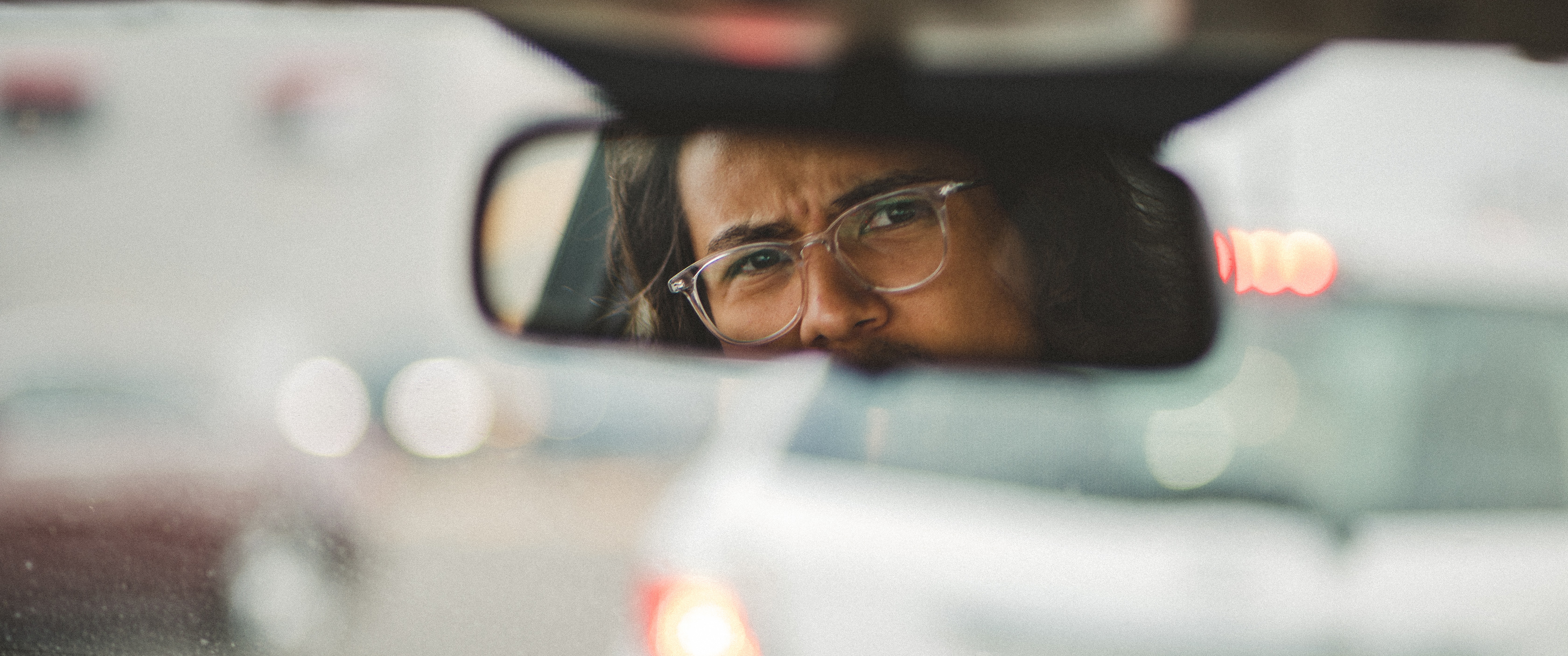 man squinting as he looks in a car's rearview mirror