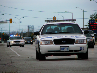 تظهر صورة فوتوغرافية سيارتين للشرطة تقودان، إحداهما بأضواء ساطعة.