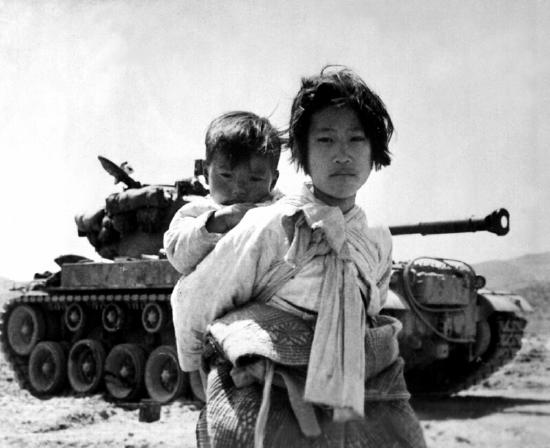 Korean girl carrying a baby on her back in front of a war tank