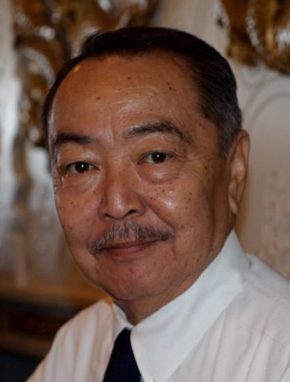 A headshot of Aoki with a mustache is looking at the camera and wearing a black tie