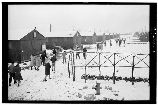 Several inmates walking by barracks in the snow covered camp