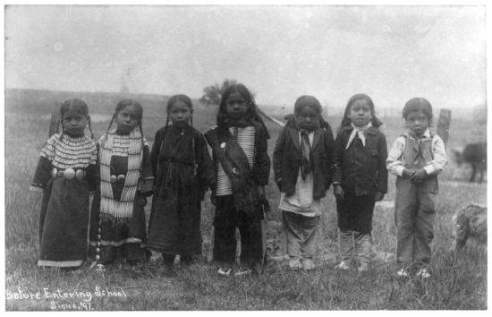 Seven Native American children with four in traditional clothing and three in European American clothing