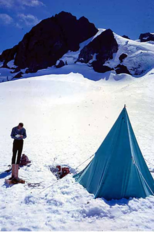 A person is shown taking notes outside a tent in the mountains