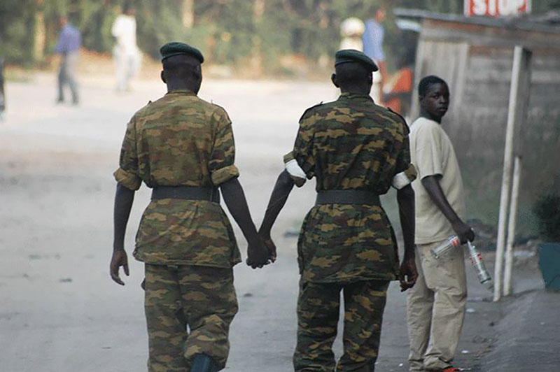 Two soldiers in uniform are shown from behind walking and holding hands.