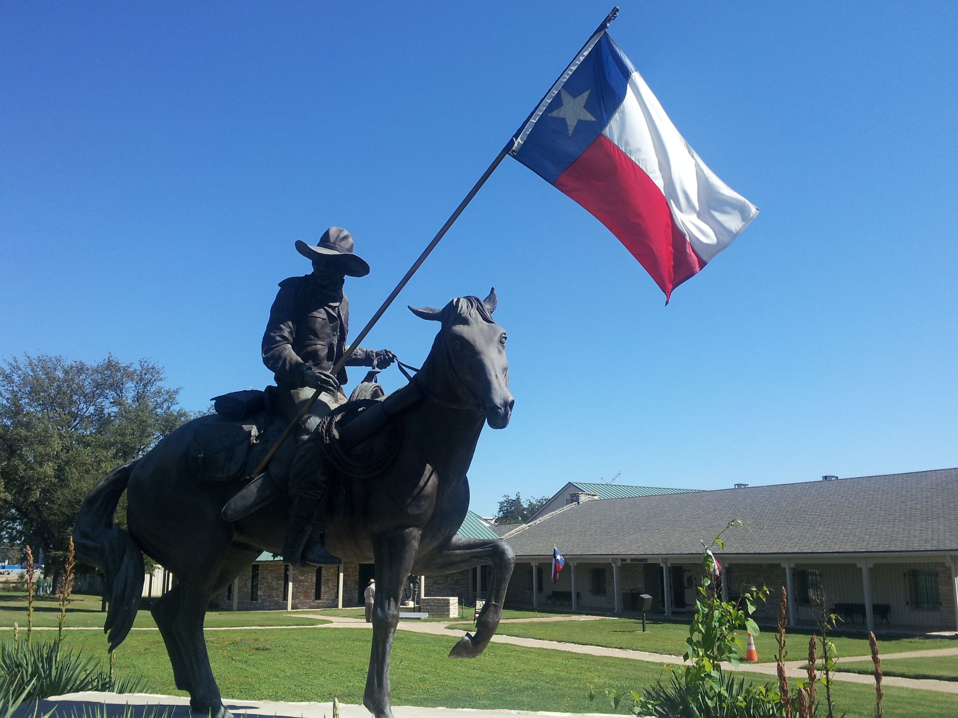 statue of a Texas Ranger on a horse, holding a Texas flag, turning his head over the right shoulder