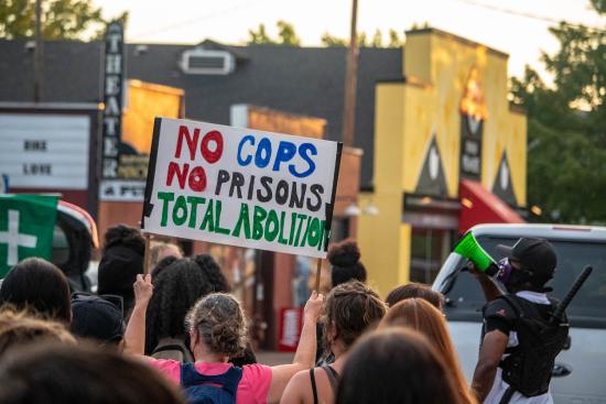 Protesters marching and one person holding a sign reading No cops no prisons total abolition