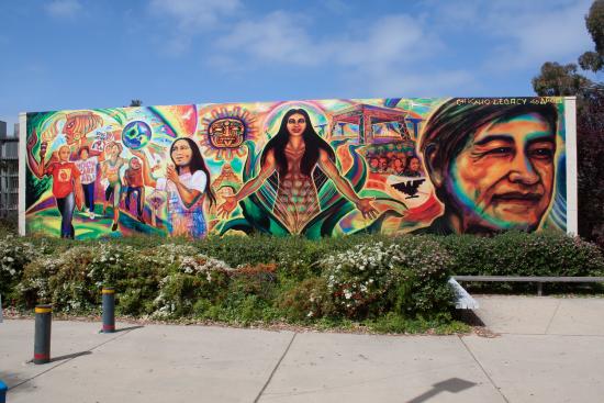 mural of Cesar Chavez on the right, a woman coming out of a corn husk in the middle, people marching to the left
