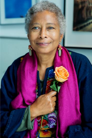 Walker with short gray hair wearing a purple scarf is holding an orange rose