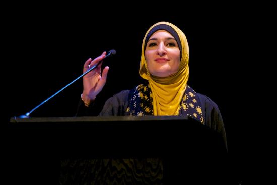 Sarsour at a podium wearing a yellow hijab, smiling