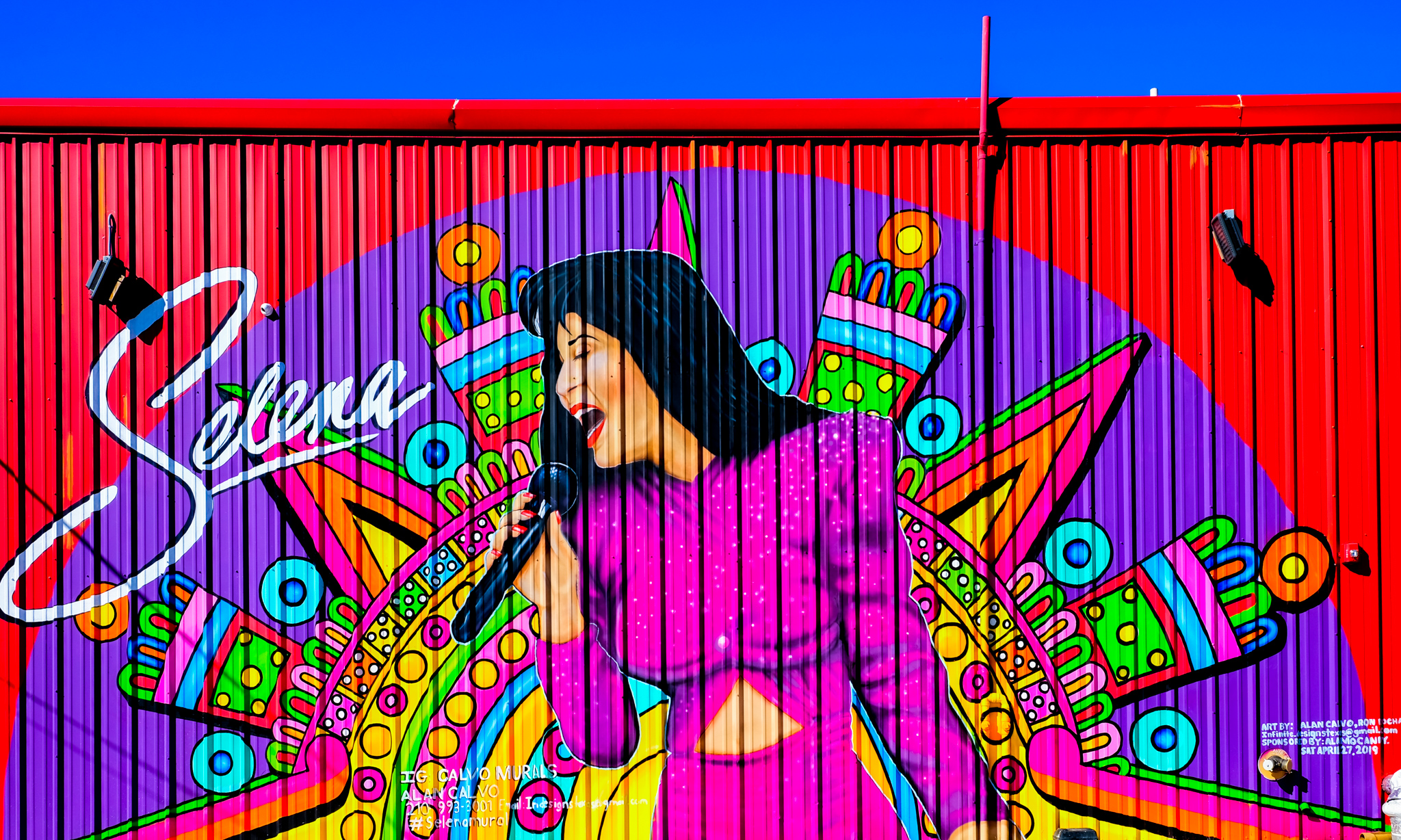 Selena singing into a microphone, against a background with bright colors and Aztec-inspired pattern.
