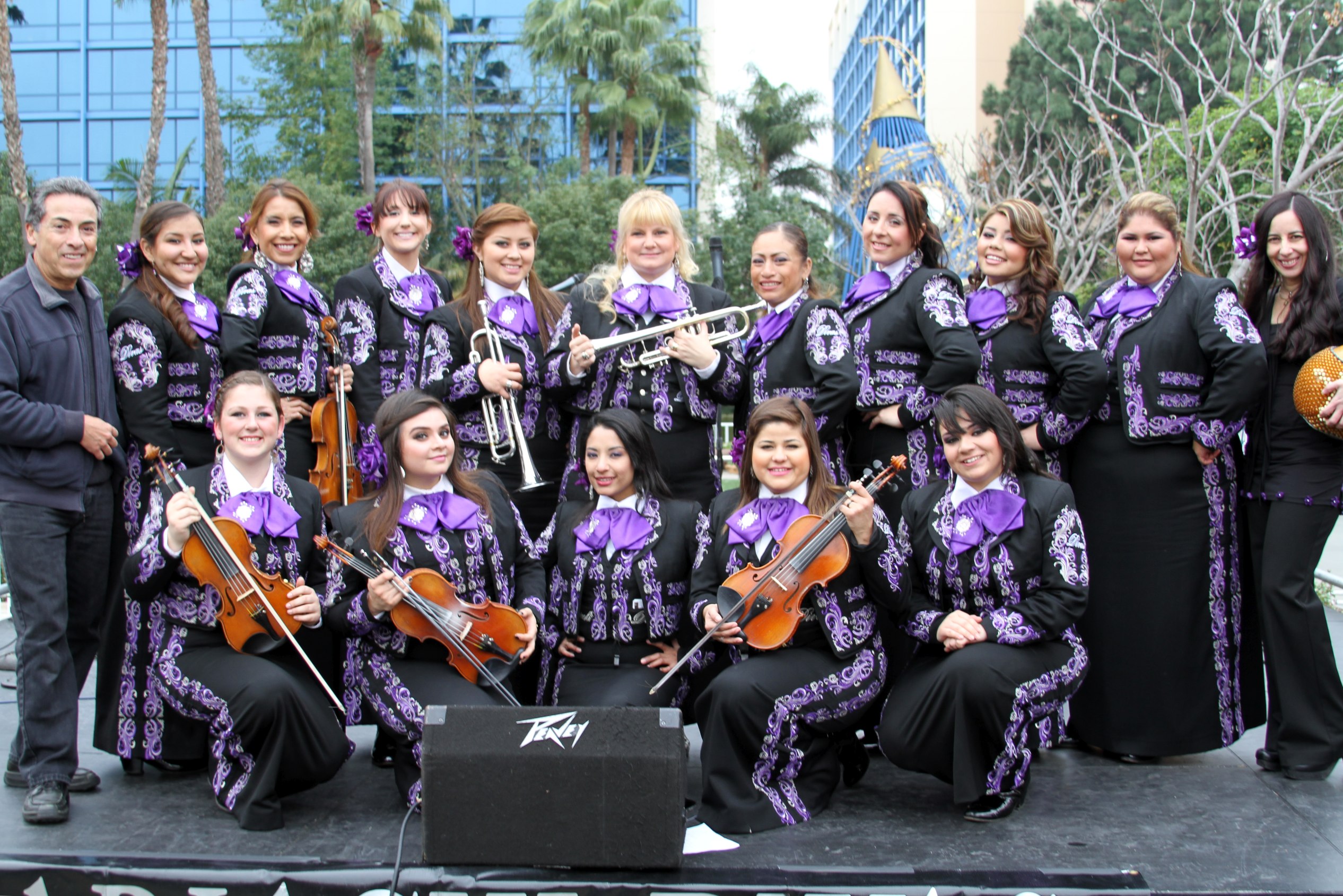 An all woman mariachi band, dressed in traditional attire with purple accents, holding their instruments and smiling
