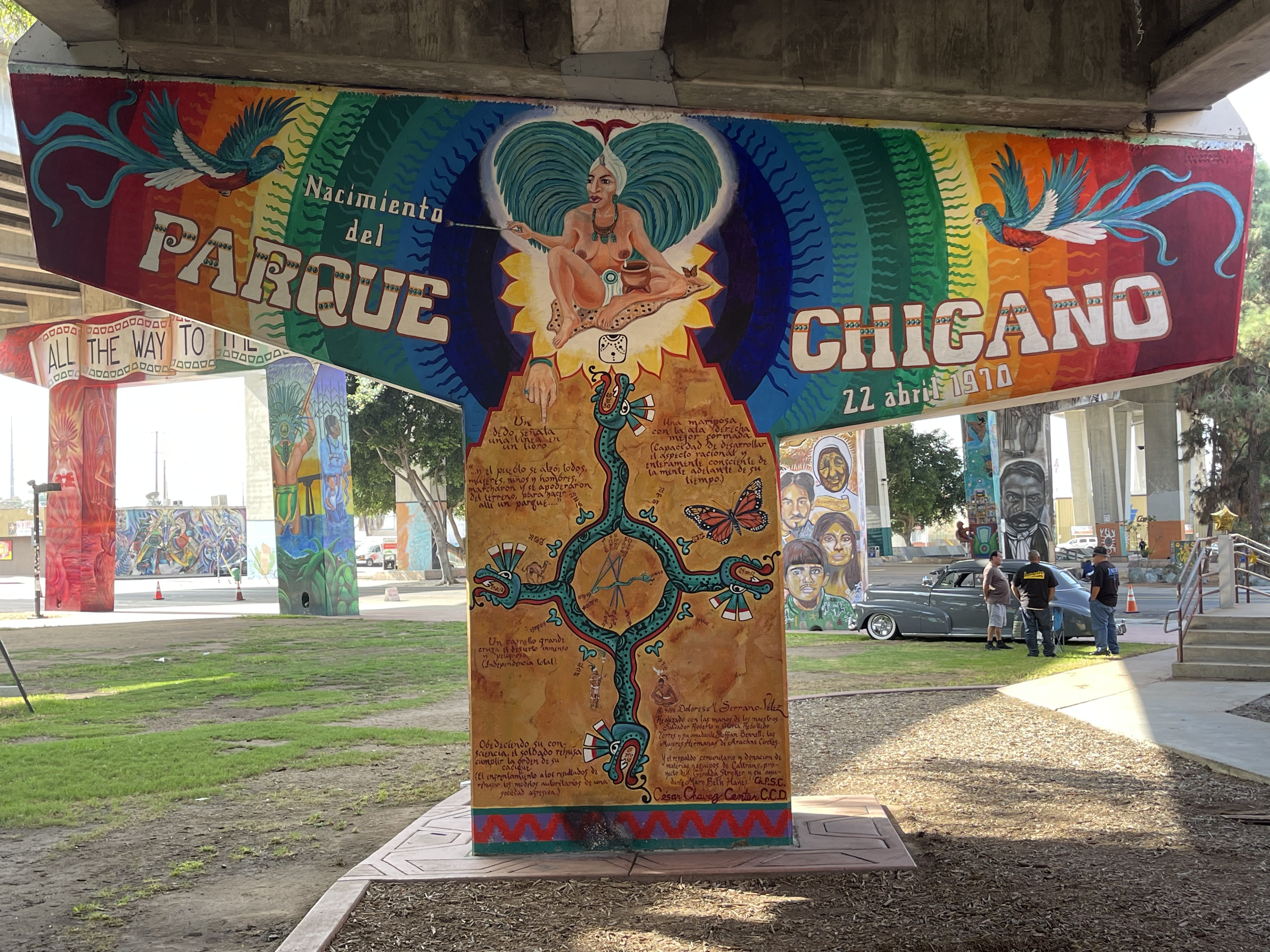 A mural with Indigenous style artwork and a four-directional serpent and a goddess figure against a rainbow background.