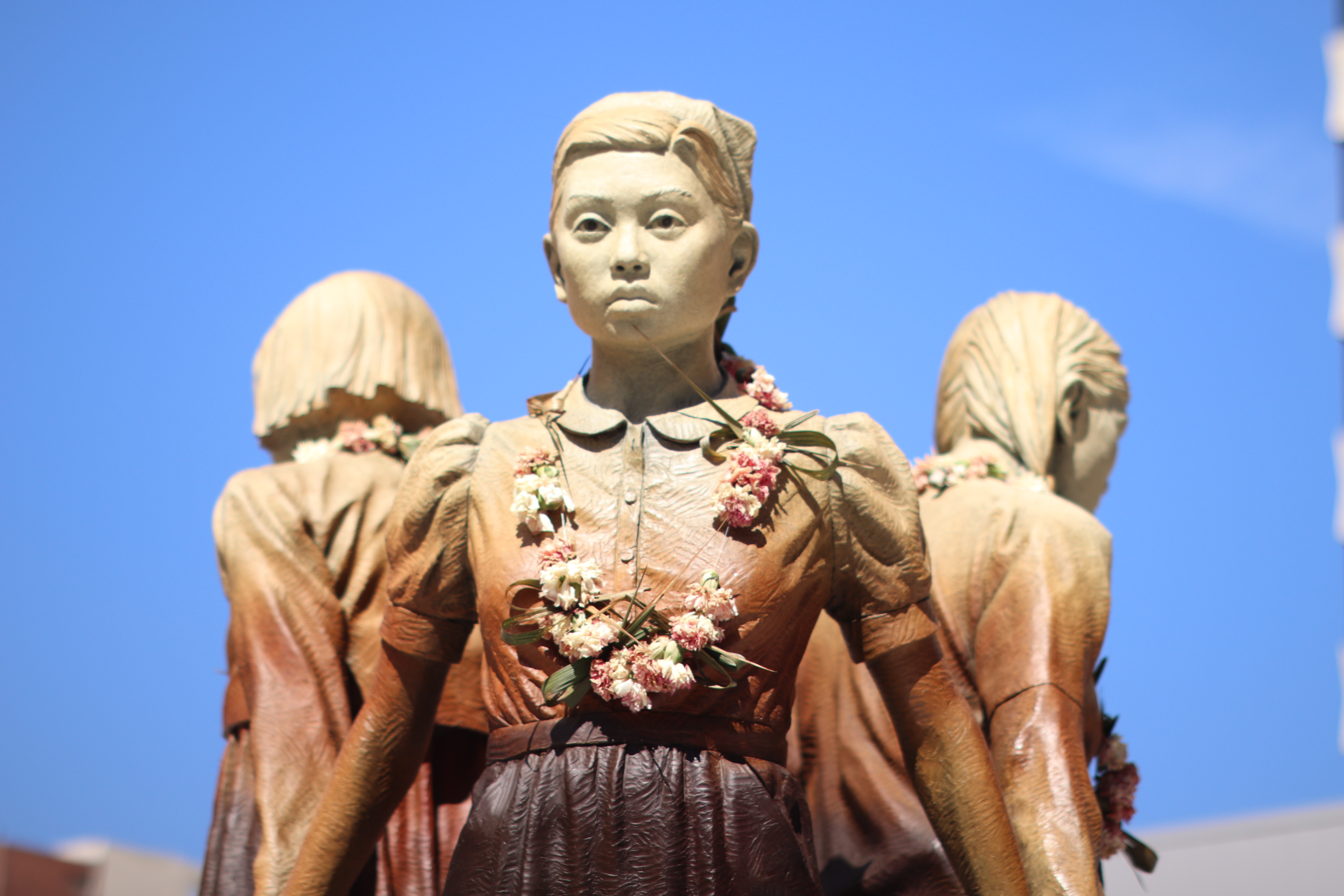 bronze statue of a girl wearing a blouse, holding hands with other two girls, wearing a flower lei necklace