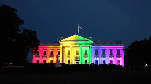 Photograph of the White House at night illuminated by lights making a rainbow pattern across the building.
