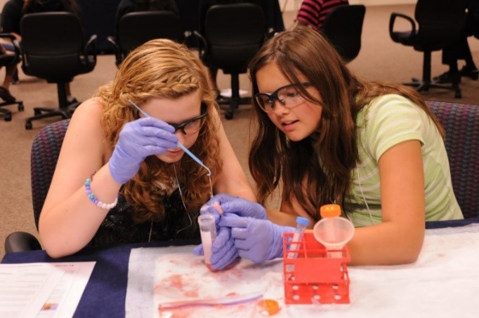 Two girls wearing latex gloves and protective goggles perform a science experiment