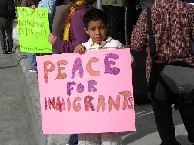 A Brown child holding a sign saying Peace for immigrants as part of a protest.