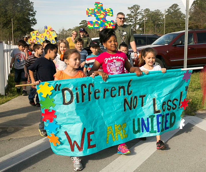 Three children carrying a sign saying "different not less, we are unified" and other people following