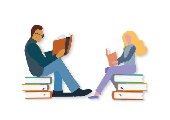 Two people studying, each sitting on a pile of books. They are facing one another. 