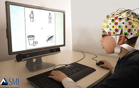 照片描绘了一个人看着电脑屏幕并使用键盘和鼠标。 该人戴着一顶白色的帽子，上面覆盖着电极和电线。